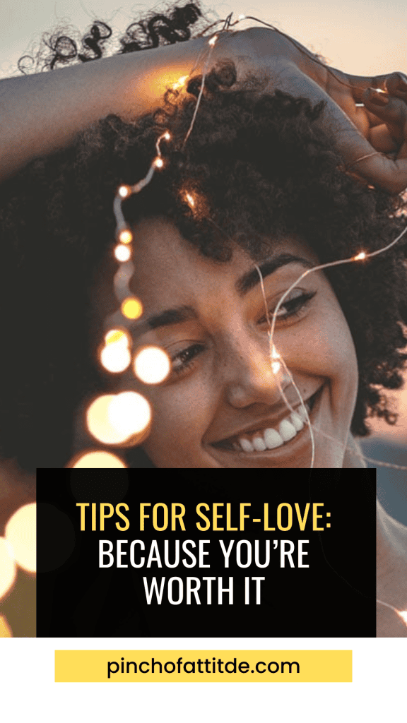 Pinterest - Pin with title "Tips for Self-Love: Because You're Worth It" showing a smiling woman with curly hair holding string lights near her face with a warm sunset background.