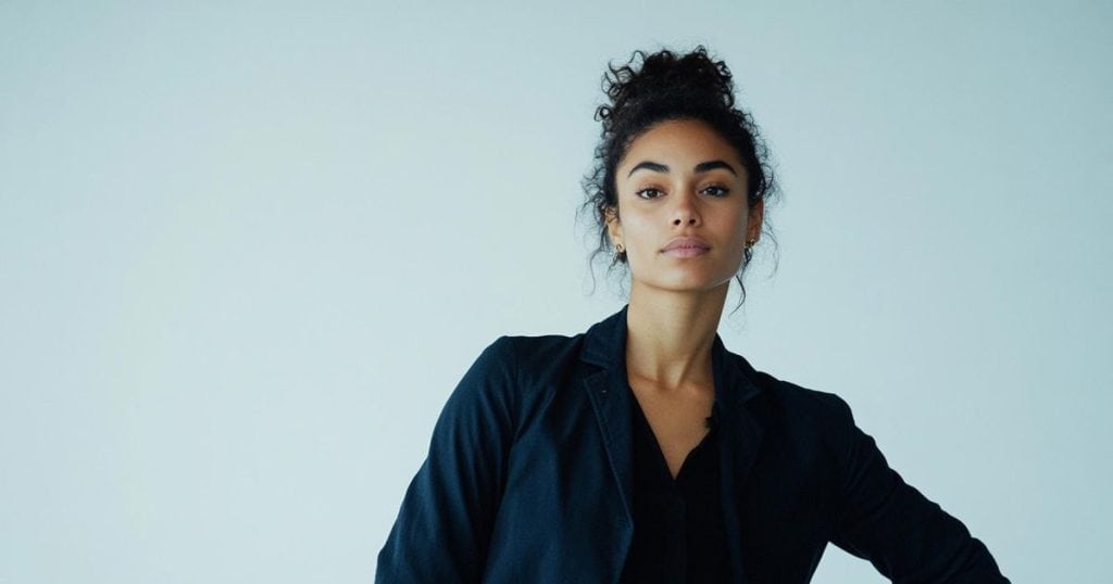 a beautiful woman with her hair in bun dressing in black suit with one hand on her hip looking fierce.