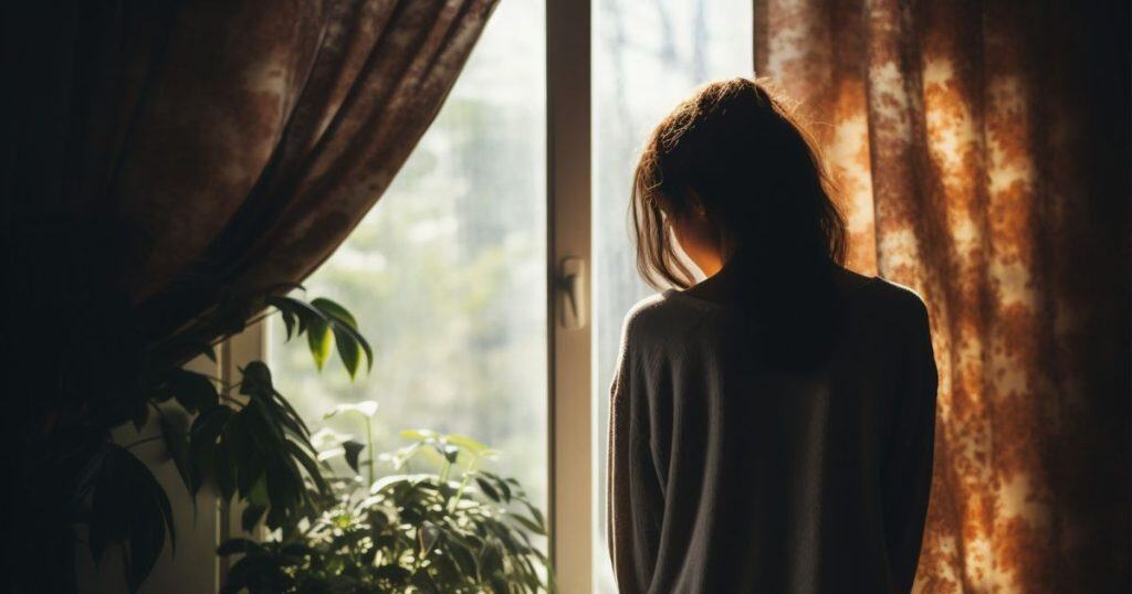 a woman looking outside of the window feeling hopeless as she's all alone after leaving her narcissistic partner to create a better life for herself.