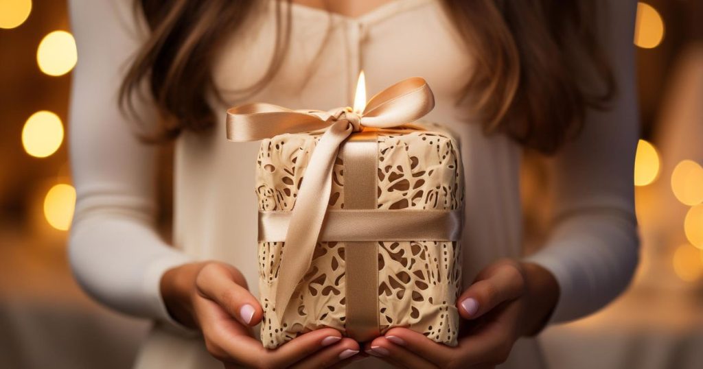 a woman holding a white gift with candle on top.