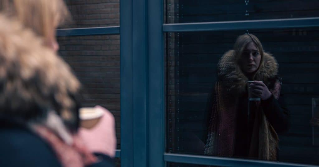 A young woman sadly looks at her reflection in a window in winter season.