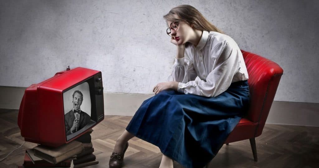 Woman looking very bore wathing TV alone sitting on a red chair.