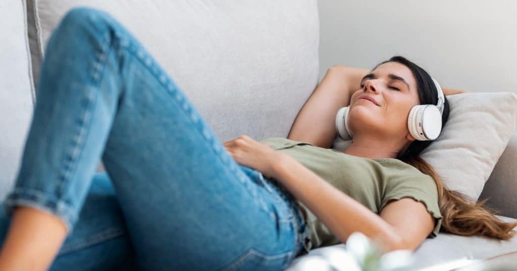 Shot of beautiful kind woman relaxing while listening music with headphones lying on couch at home.