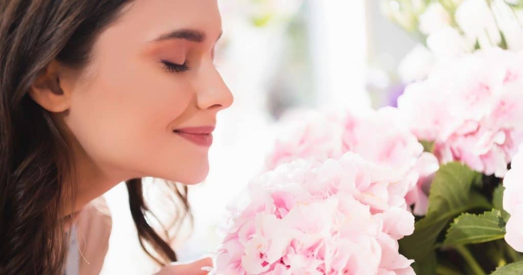 Side view of smiling woman with closed eyes smelling hydrangeas.