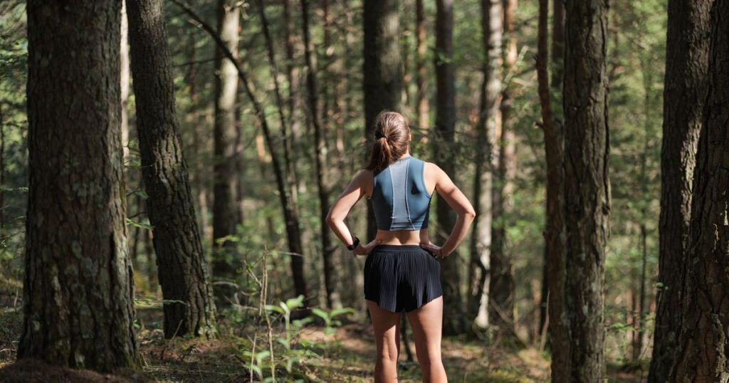 a woman dressing in jogging gears standing alone with forest full of big trees looking up in the sky feeling free from narcissist's control in her life.
