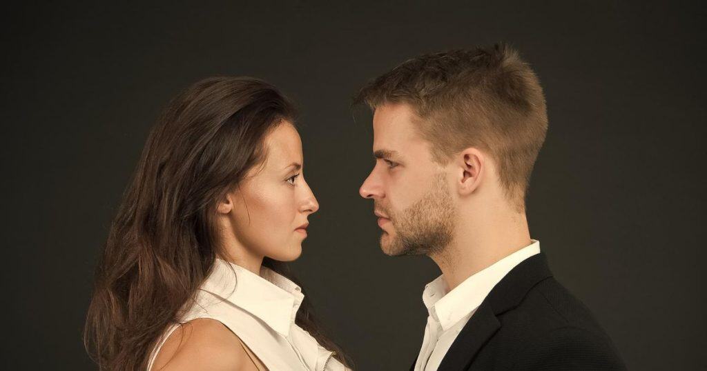 a woman and a man facing each other both wearing business casual and looking very serious.