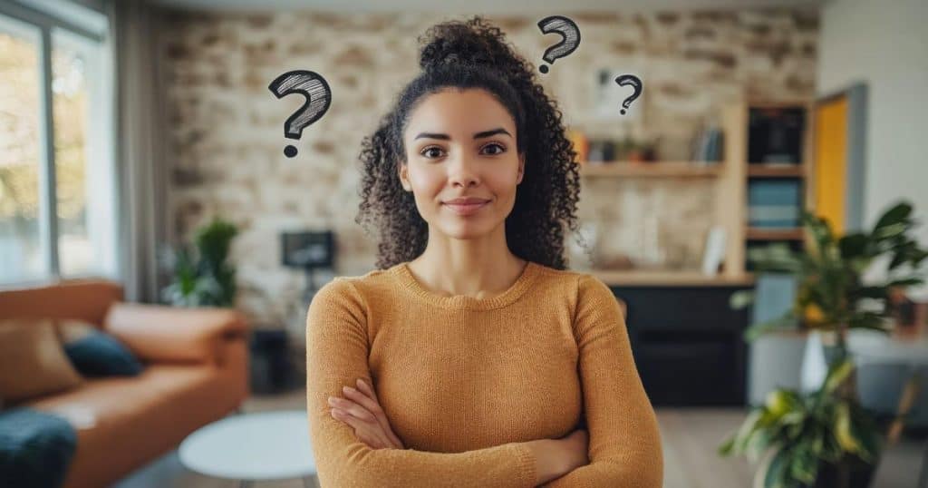 a coloured woman standing with her arms crossed wearing a yellow knitted shirt with question marks around her head feeling happy to learn new ways of dealing with her flying monkeys.