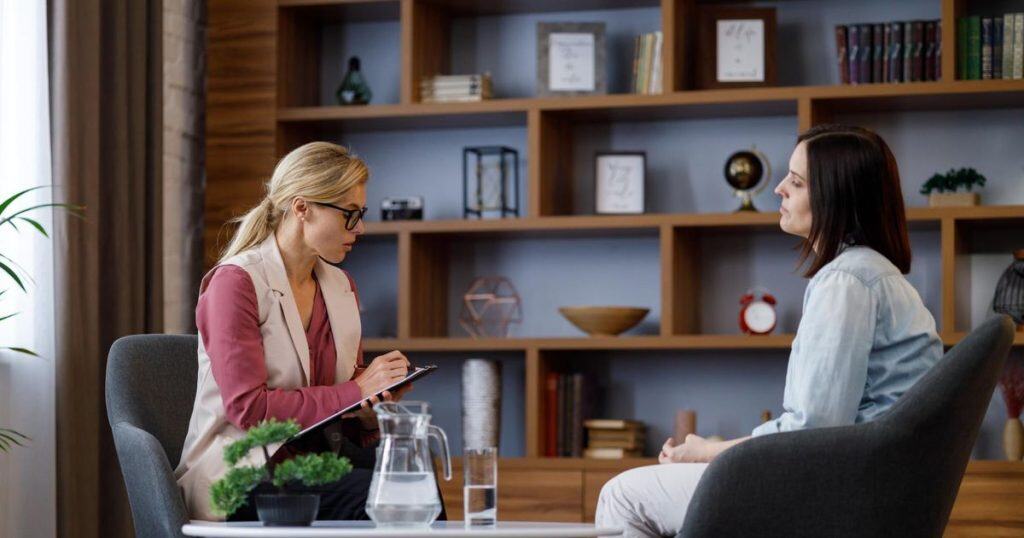 a sitting wearing jean shirt with short hair sitting in a well-decorated room with her therapist while talking aobut fake apologies from narcissistic partner.