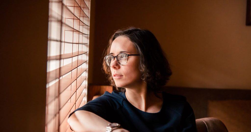 a portrait of a dreamy woman with short hair sitting in a chair close to the window staring away so deeply.