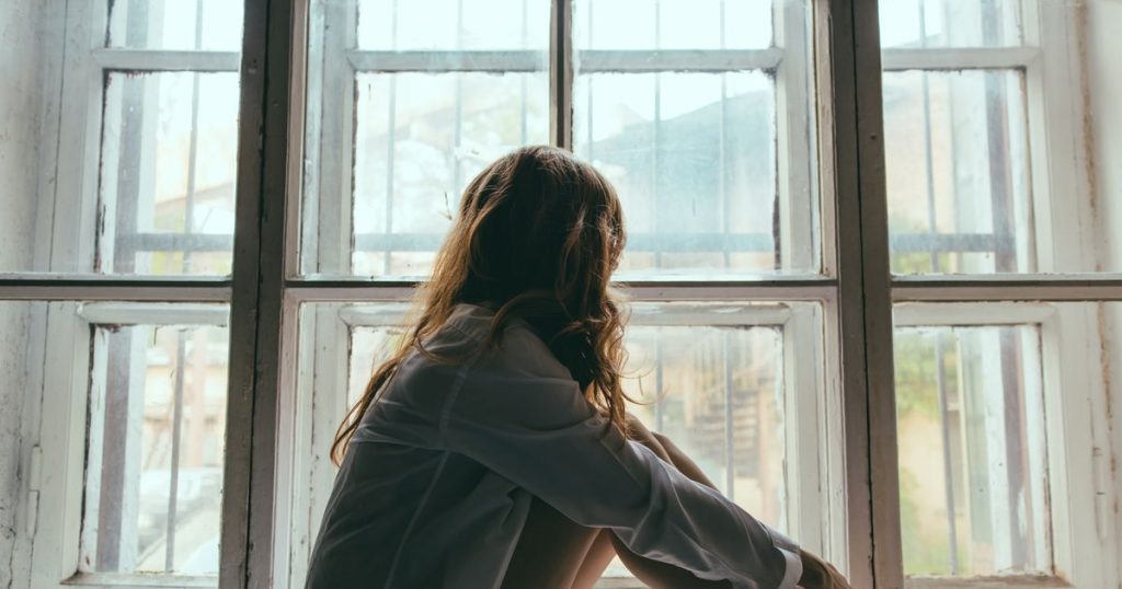 a woman wearing a white shirt sitting on a wooden floor looking outside her window with her red hair.