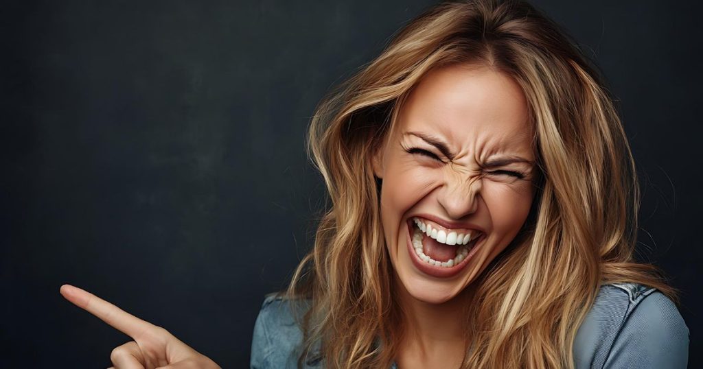 a woman wearing a blue shirt with long blond hair pointing to her left laughing as she doesn't believe the apologies she got from her narcissistic family.