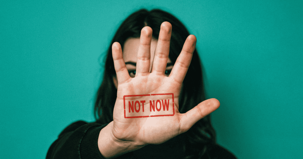 A woman stands against a teal background, holding up her hand with the words “NOT NOW” stamped in red across her palm. This is a visual metaphor for setting firm boundaries and refusing narcissistic control.