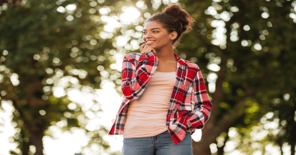 A woman stands outside smiling softly to herself, finally free from the roles that once kept her small.
