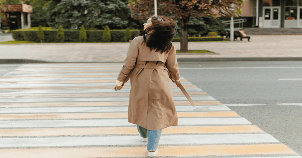 A woman walks away across a crosswalk with her head turned and hair flipping back, a quiet act of reclaiming her power and choosing herself.
