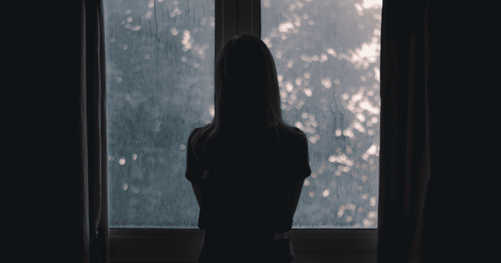 A woman stands by a rainy window, wondering why she keeps ending up in the same emotional loop.
