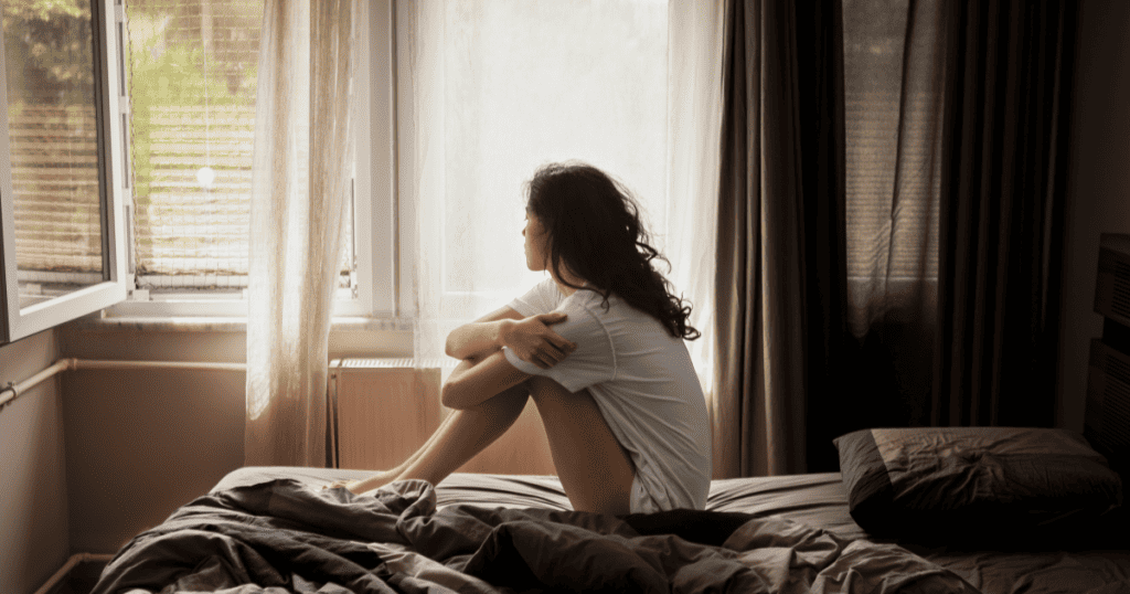 A woman stares out the window, confused why peace feels more uncomfortable than chaos.