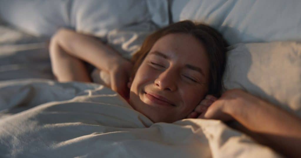 a woman smiling with her eyes close as she's waking up in the morning lying in her bedroom.