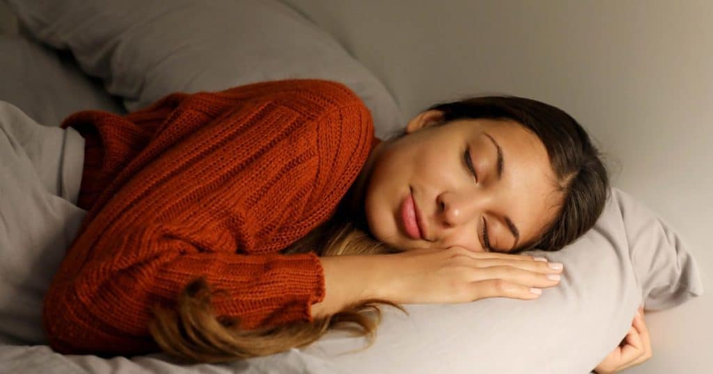 Young woman sleeping peacefully on the bed wearing a red knitted sweater with her brown hair falling on her shoulders.
