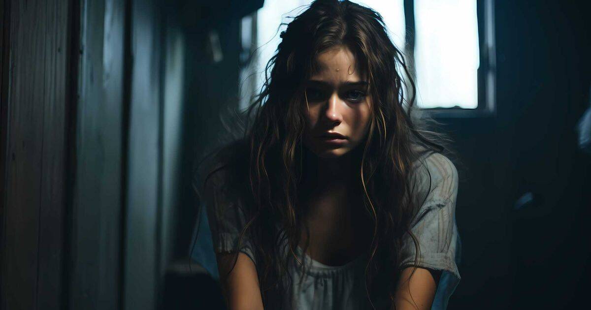 A young woman sits on the floor in a dimly lit space, her face marked by exhaustion and pain, embodying the raw vulnerability and emotional weight often misjudged or dismissed by society in trauma survivors.