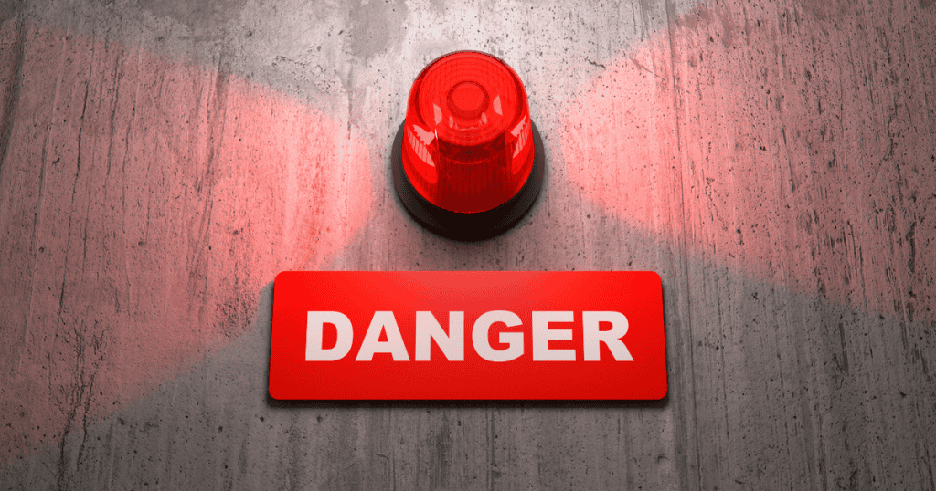 A glowing red siren flashes above a bold danger sign, symbolizing the undeniable physical red flags that expose a narcissist no matter how well they try to mask them.