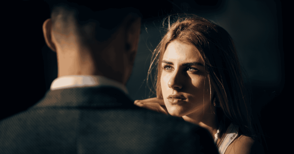 A woman staring intensely at a man in shadow, reflecting the hard-earned clarity that comes with learning harsh truths about narcissists.