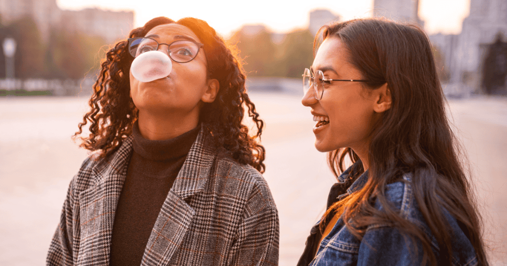 Two women laughing together while blowing bubble gum, perfectly capturing the playful narcissist dismissal.