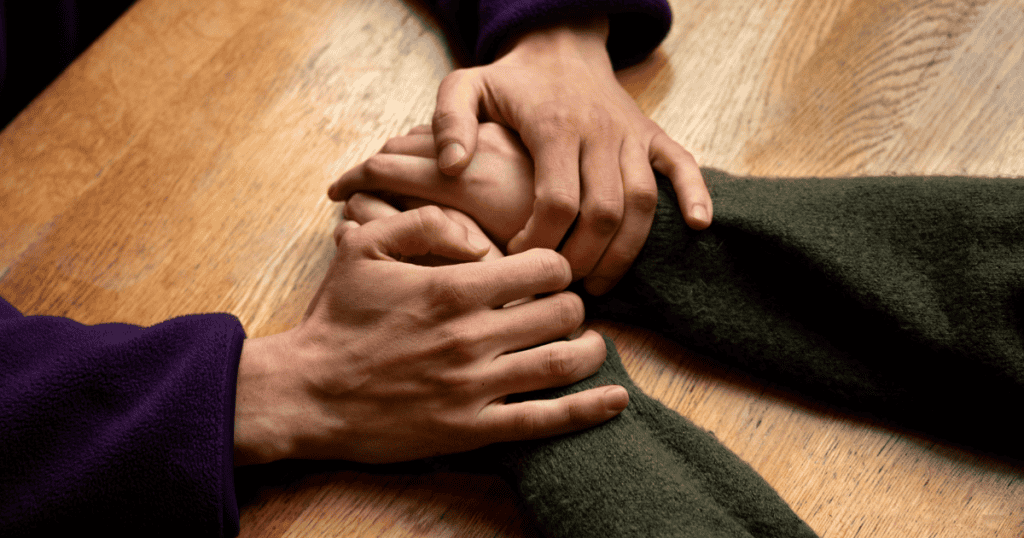 Two people clasp hands across a wooden table, symbolizing receiving support while maintaining personal power.