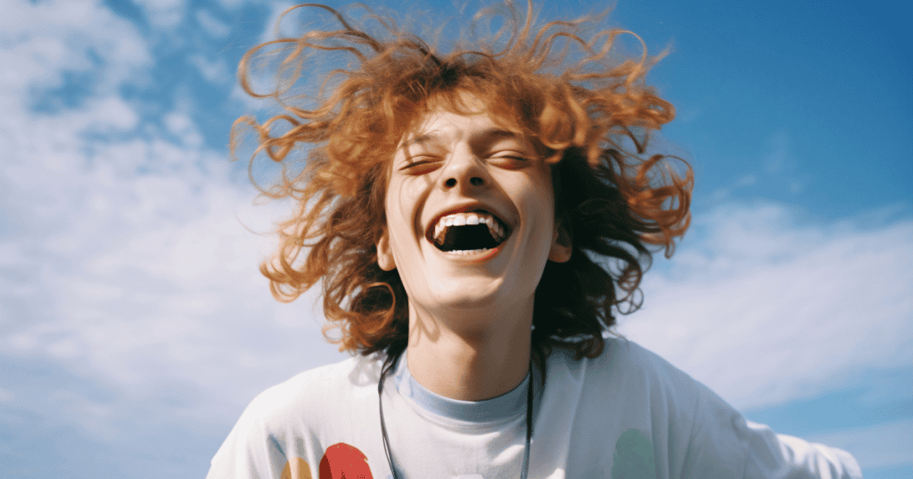 A young person laughs freely under a bright blue sky, their hair wild in the wind, a striking symbol of how choosing forgiveness without reconciliation can release the weight of bitterness and open the door to real freedom.