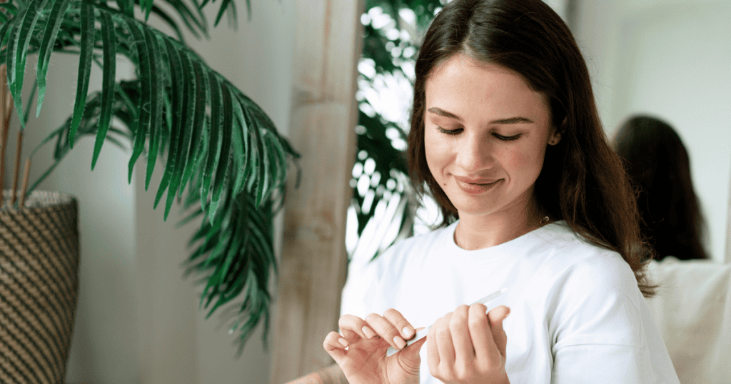 A smiling woman in a white shirt sits near a plant while writing in a notebook, illustrating how this empowering mindset appears in everyday life.