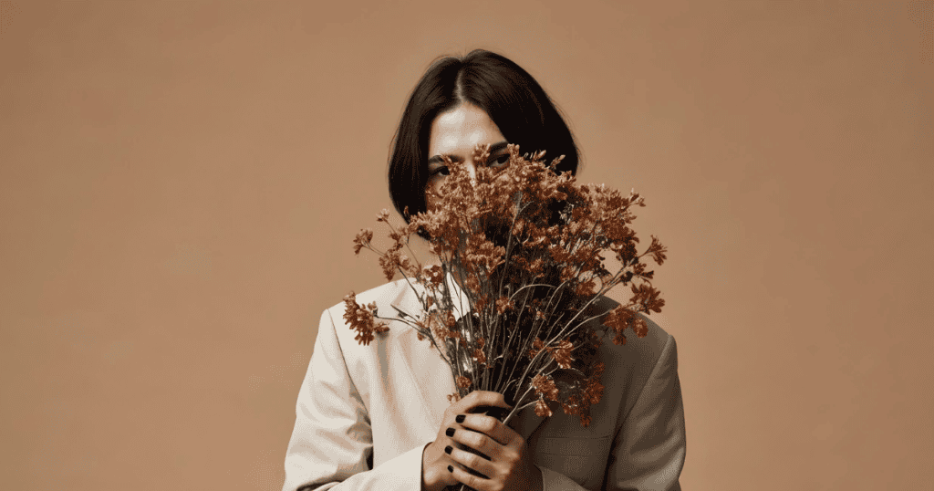 A person in a beige suit holds dried flowers up to partially cover their face, symbolizing how to turn reclamation into an advantage against narcissists.