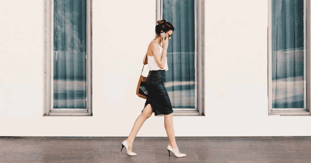 A confident woman walking away while on the phone, dressed in a sleek skirt and heels, symbolizing the quiet power of stepping out of toxic energy instead of engaging with it.
