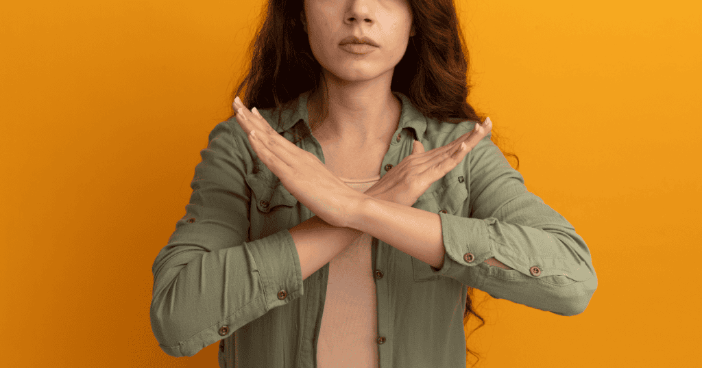 A woman standing firmly with arms crossed in an X, symbolizing a clear boundary and refusal to engage in toxic communication.