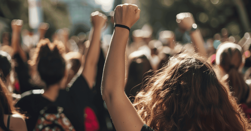 A crowd of people raise their fists in solidarity, representing resistance against the harmful glorification of suffering for the sake of family loyalty.