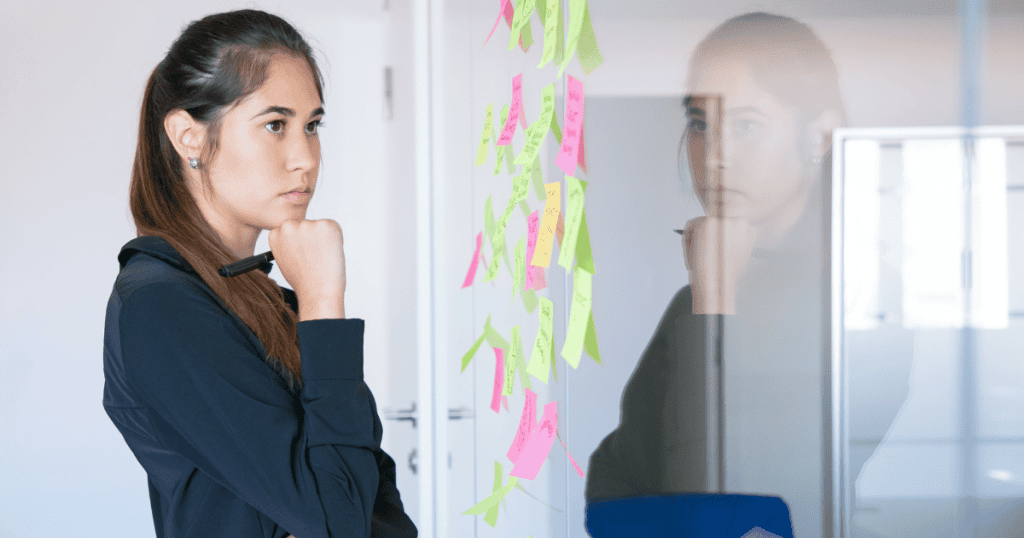 A focused woman stands in front of a glass wall covered with colorful sticky notes, representing the strategic mindset that weakens a narcissistโs control.