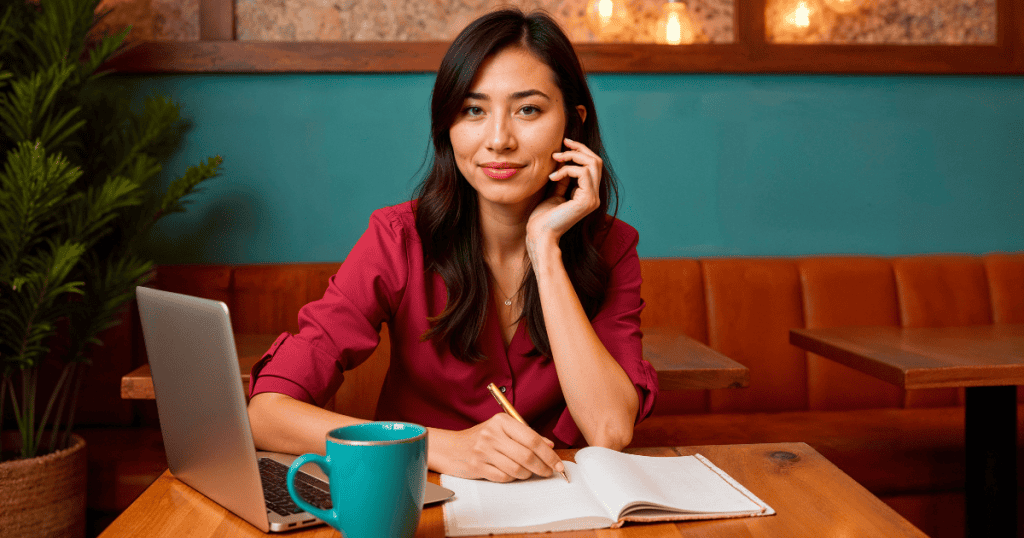 A woman sitting at a café table with a notebook, pen, and laptop, looking confident as she documents, symbolizing the moment her records of narcissistic abuse became the proof that set her free.