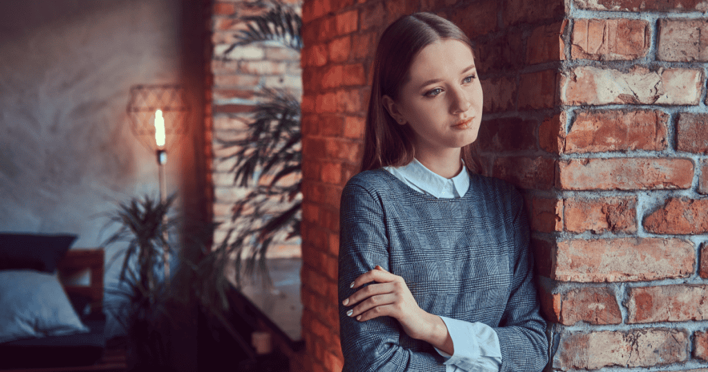 A woman leaning against a brick wall with a thoughtful expression, symbolizing the realization that true loyalty isn’t about enduring pain in silence.