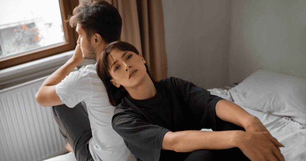 A woman leans back-to-back with a distant man in a bedroom, reflecting the shift that happens when you stop trying to change a narcissistic relationship.