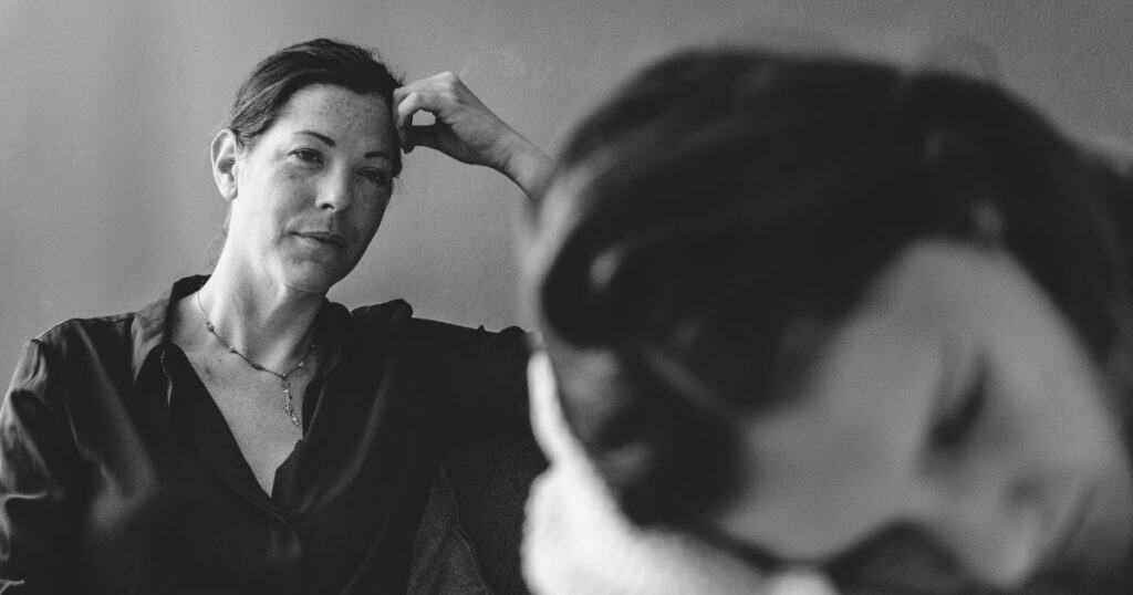 A black-and-white photo shows a focused woman watching another person blurred in the foreground, illustrating the moment of witnessing a narcissistโs fallout.