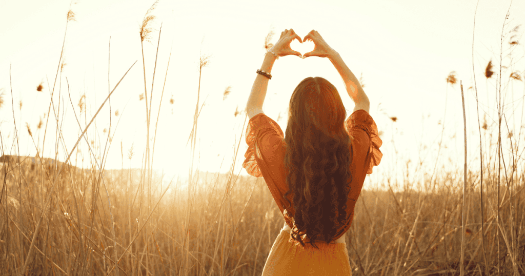 A woman stands in a sunlit field making a heart shape with her hands, symbolizing the freedom and strength that comes from choosing yourself over a narcissist.