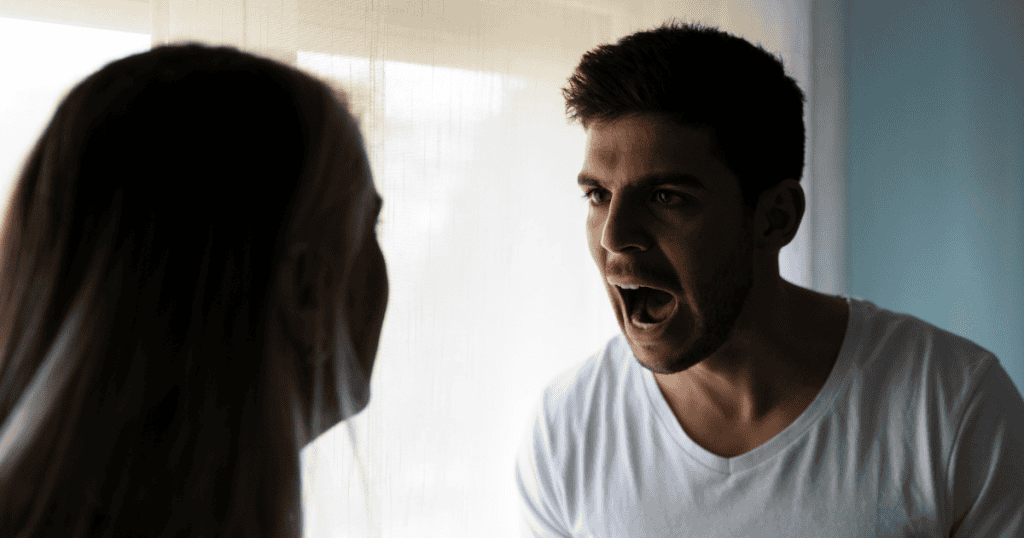 A man in a white shirt shouts at a woman in silhouette, showing an angry man confronting someone he ultimately fears.
