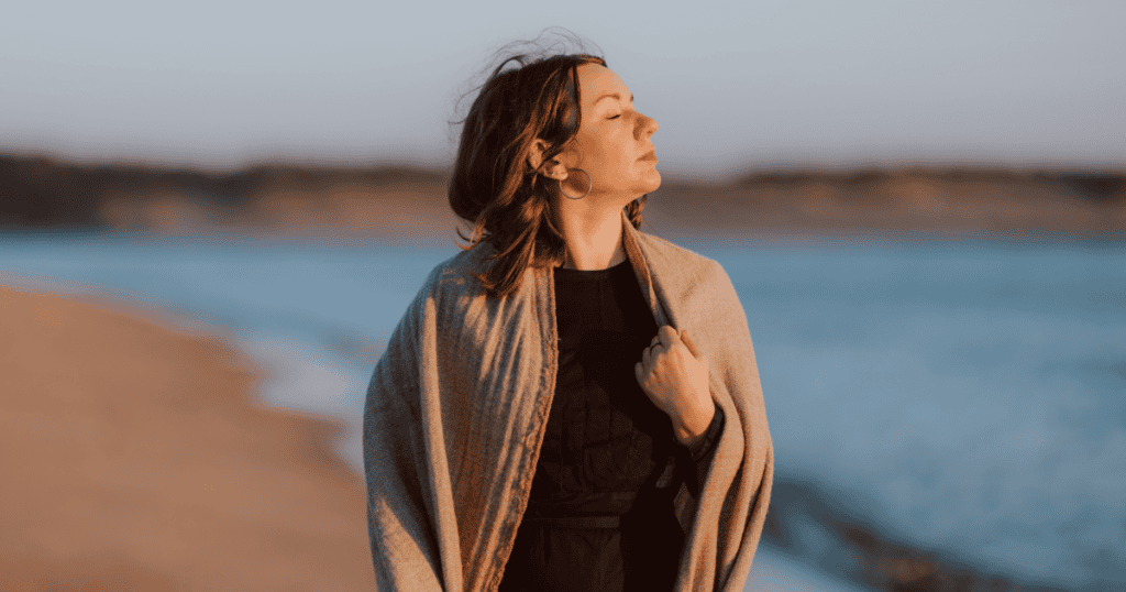 A woman standing calmly by the water with her eyes closed, embodying the freedom of choosing peace over family obligation.