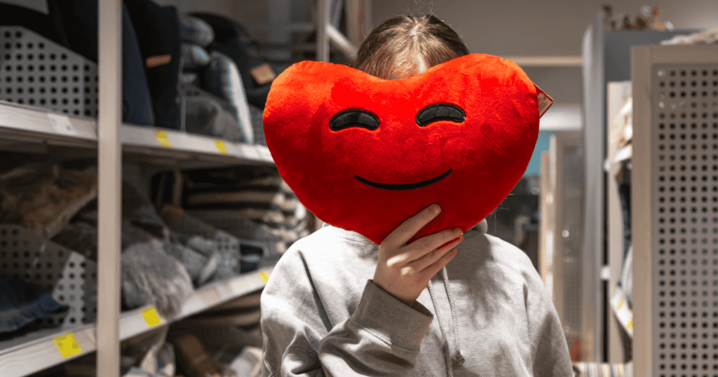 A person holding a smiling heart pillow over their face, symbolizing the false concern narcissists disguise as kindness.