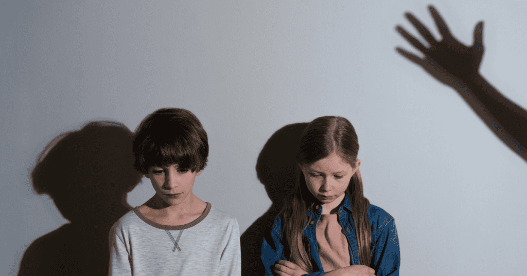 Two children standing sadly against a wall with a shadow of a raised hand looming over them, symbolizing how narcissistic parents project blame onto a chosen scapegoat.