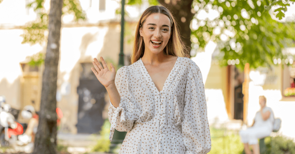 A smiling woman waving goodbye outdoors, illustrating the boundary-setting move of calmly exiting.
