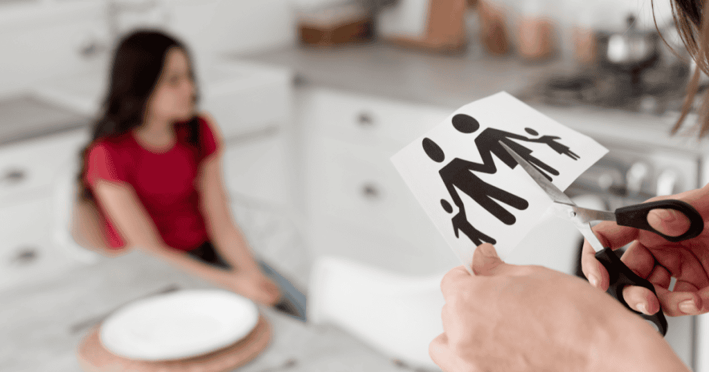 A hand cutting a paper family illustration while a child sits blurred in the background, symbolizing the painful truth that blood doesn’t always equal loyalty.