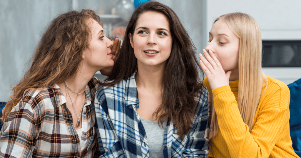 Two women whispering secrets to another woman, capturing the guarded caution you keep when dealing with a narcissist’s flying monkeys.