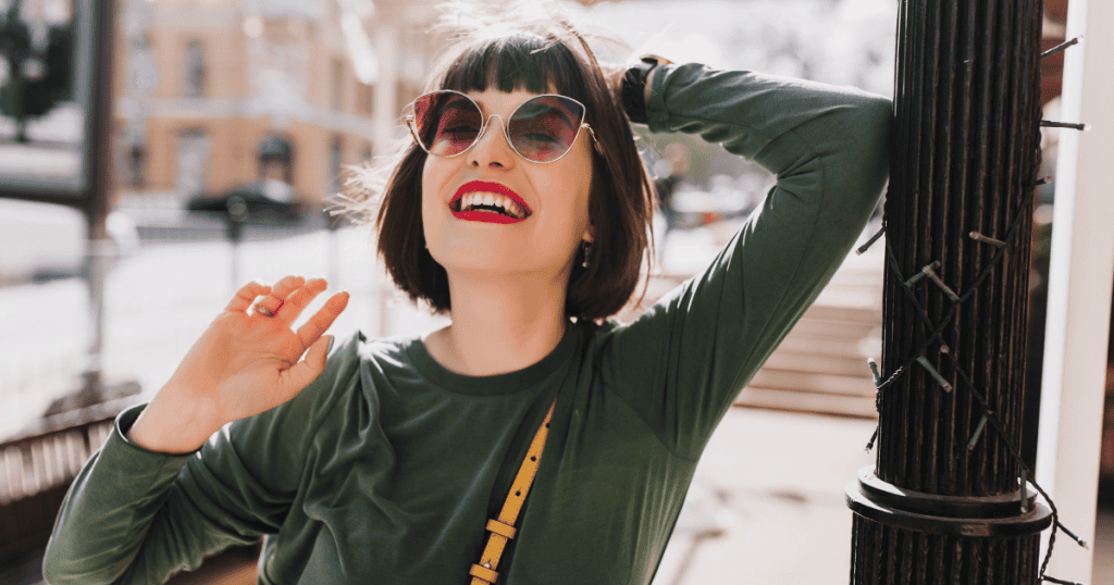 A woman beams under the sun, head tilted back in carefree laughter, her sunglasses catching the light. Every ounce of her body language declares it—she’s no longer shrinking, no longer sorry for existing exactly as she is.