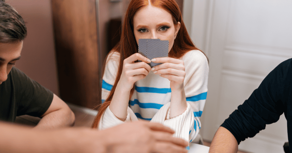 A woman holds playing cards close to her face while watching others, showing the idea of testing and spotting hidden narcissistic behavior.