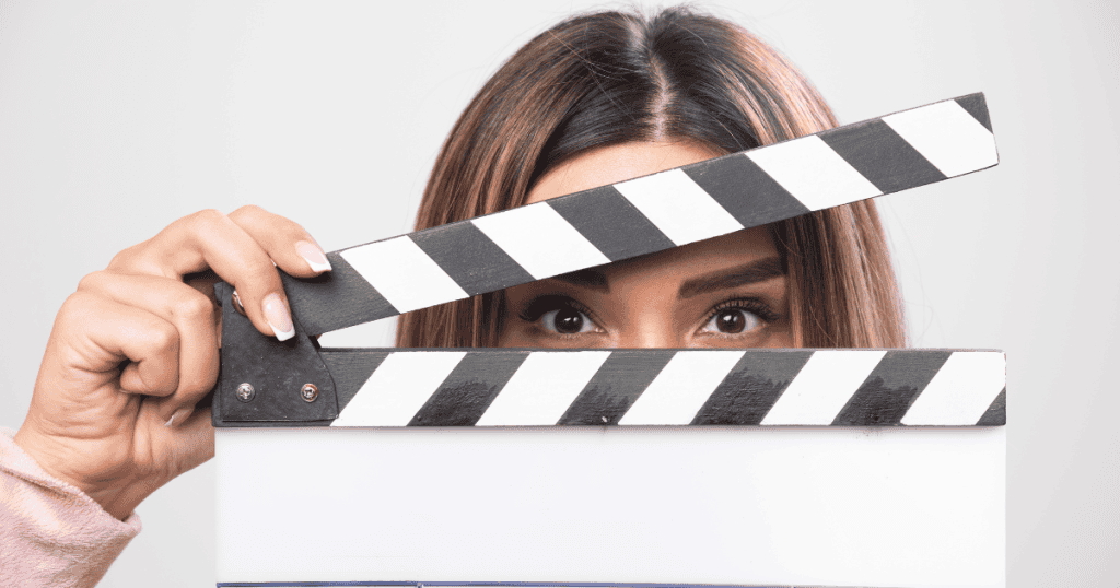 A woman holds a film clapperboard in front of her face with only her eyes visible, symbolizing the reveal of a narcissist’s true character.