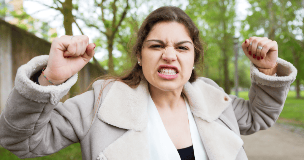 A woman clenches her fists and shouts in anger, capturing the adrenaline flood that fuels a narcissist’s dangerous rage.